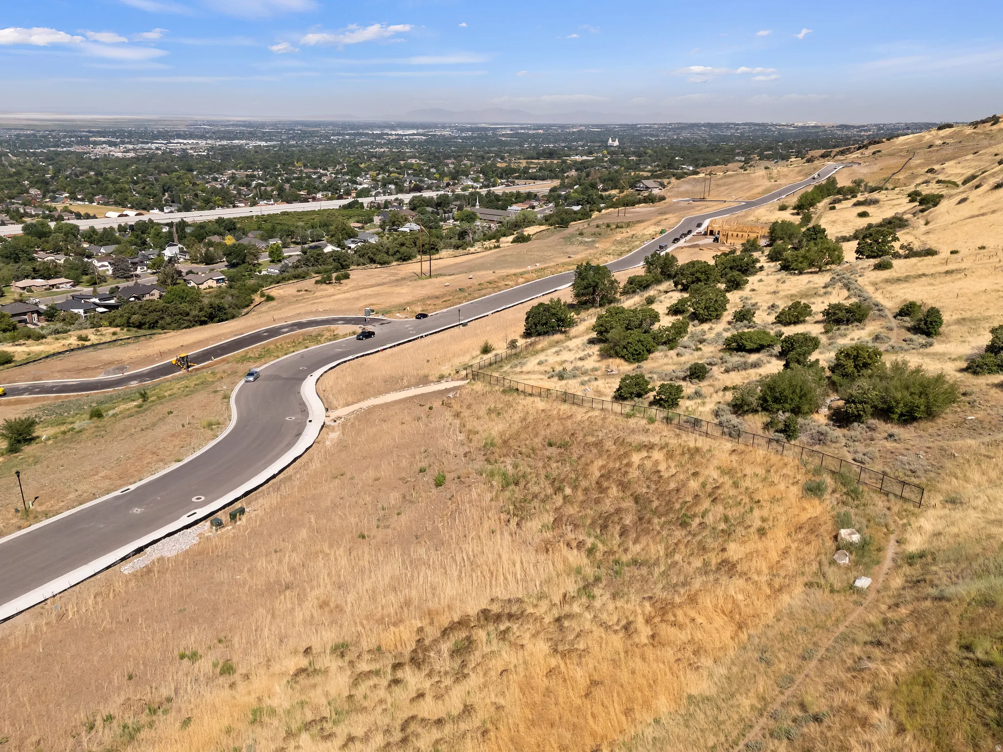 Winding paved roadway, developed residential area, distant urban landscape, natural hillside vegetation, and distant mountain range