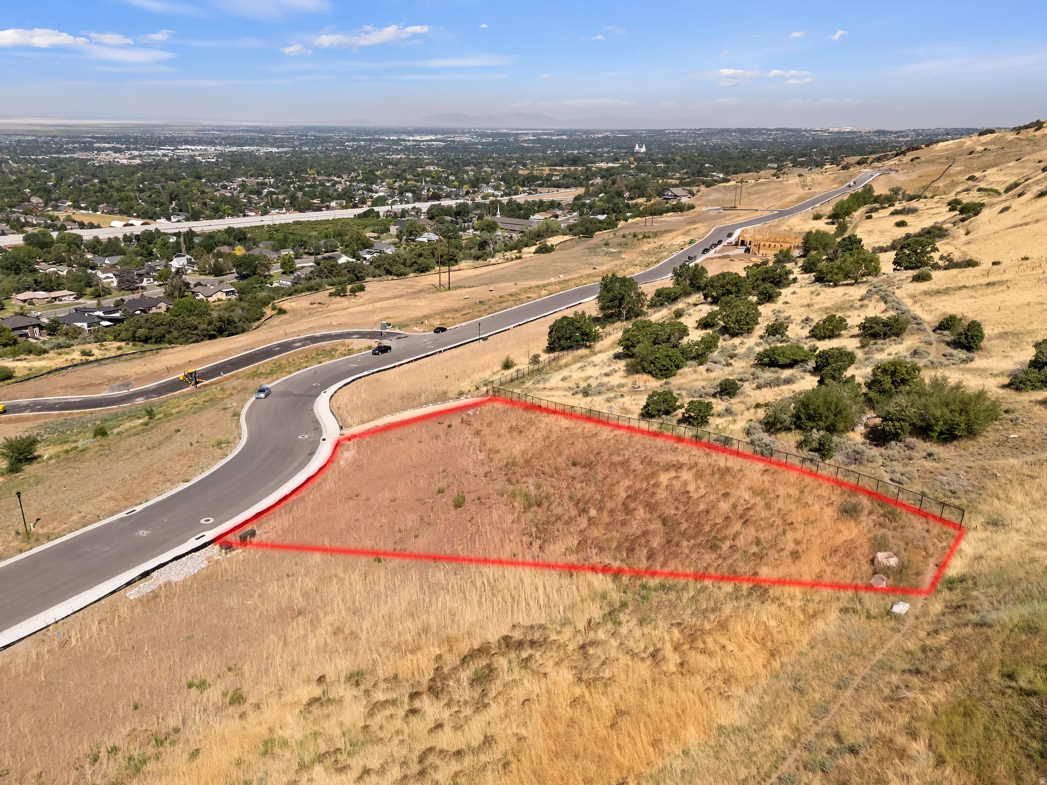 Sloping lot with natural vegetation, bordered by a fence on two sides