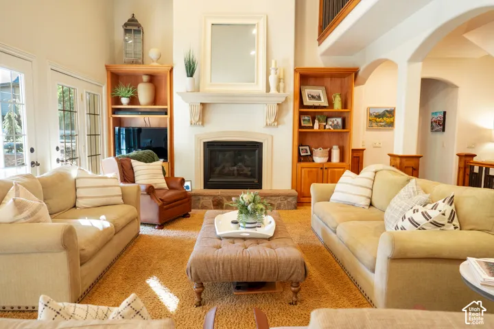 Living area featuring a fireplace with a stone hearth, custom built-in shelving, high ceilings, and archways