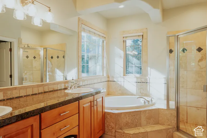 Dual sink vanity with wood cabinetry and stone-finish countertops, surrounded by a built-in jetted tub and a glass-enclosed shower featuring tiled walls