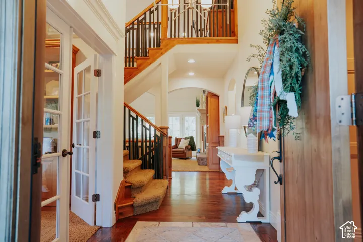 Wood-finish flooring, staircase with wrought iron balusters, French doors, and arched doorways