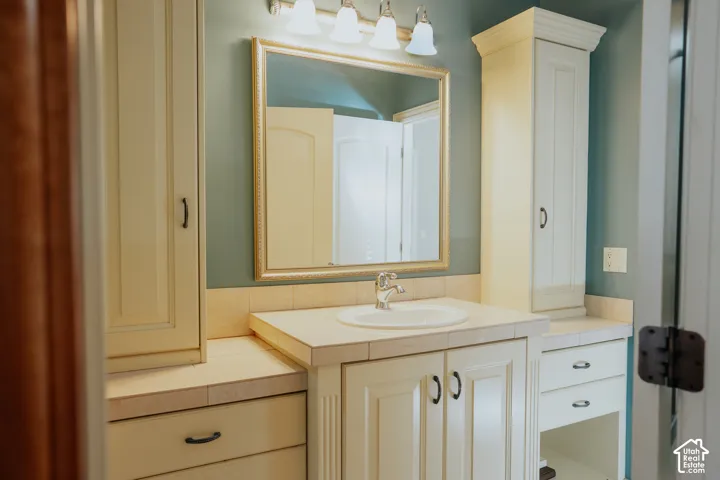 Vanity with integrated sink, tile countertop, and gold-framed mirror