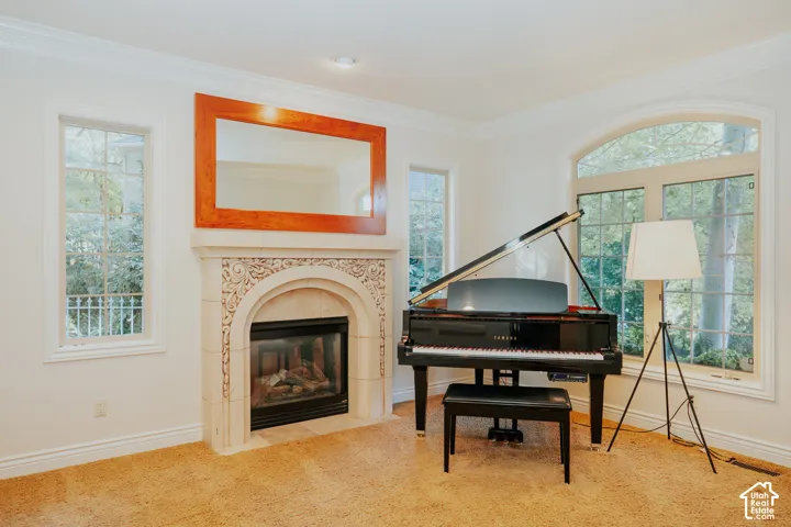 Ornate fireplace with decorative mantel, large arched window, single-pane windows with mullions, crown molding, and carpeted flooring