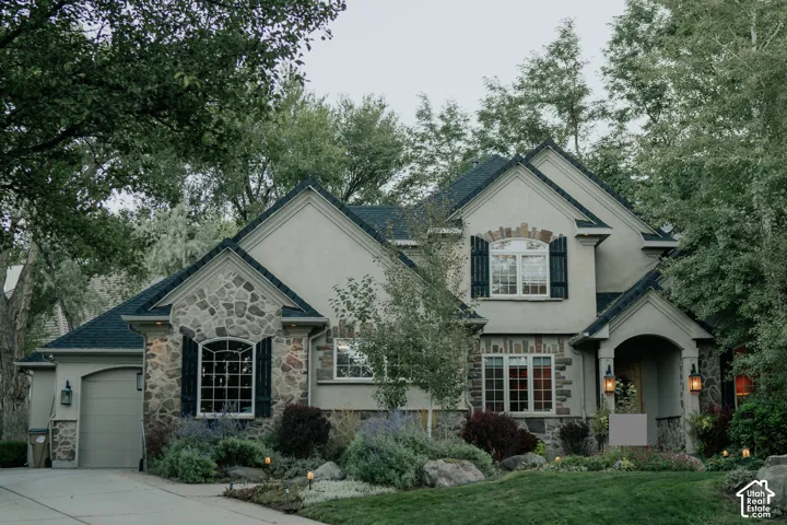 Stucco and stone exterior with dark shutters, arched entry, and a gabled roof