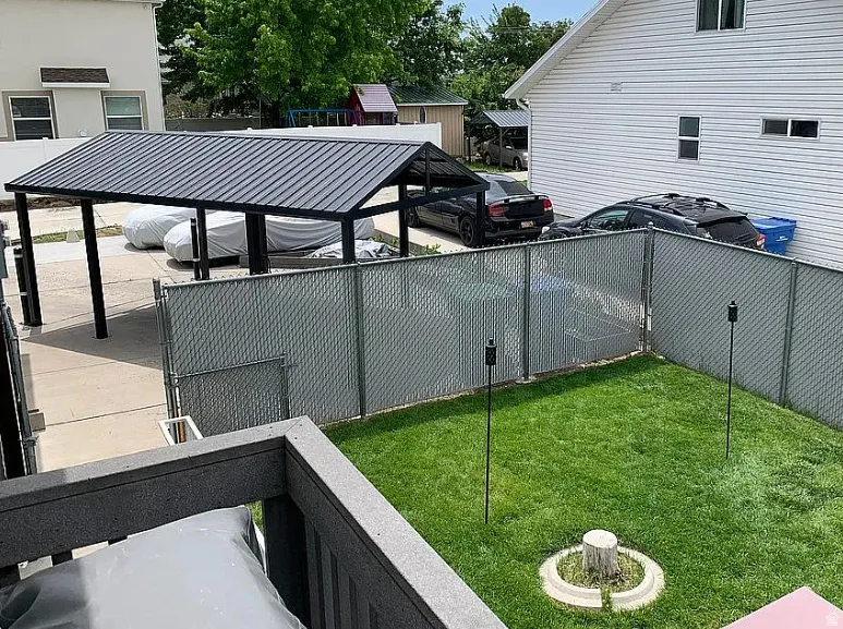 Lawn area with a tree stump feature, chain-link fencing, and a carport with a metal roof