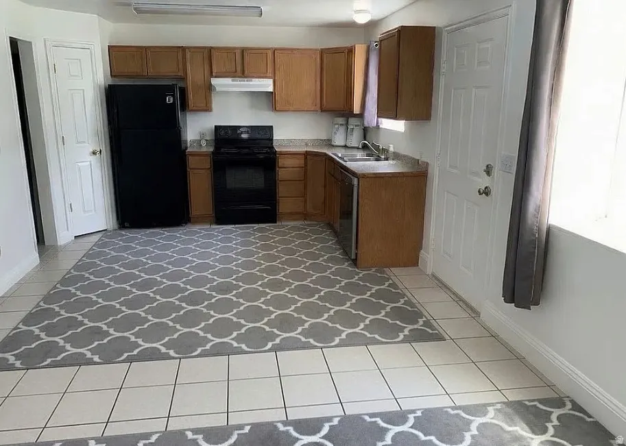 Kitchen featuring wood-finish cabinetry, black appliances, a double-basin stainless steel sink, and light-colored tile flooring