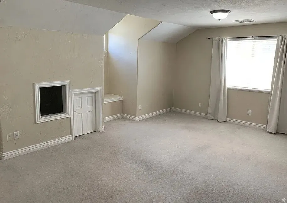 Carpeted room with a window, ceiling-mounted light fixture, and unique built-in storage or access features