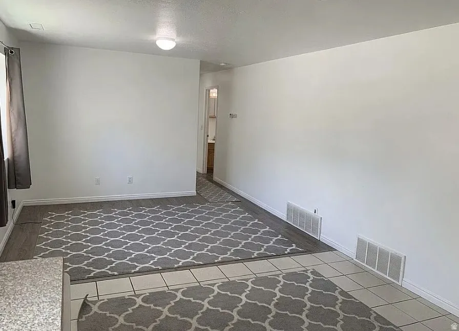 Wood-finish flooring with an inset geometric pattern rug, light-colored walls, and a semi-flush mount ceiling fixture