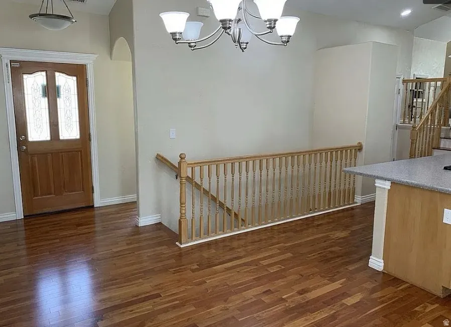 Hardwood flooring throughout, a decorative glass-paneled entry door, overhead chandelier lighting, and a wooden banister