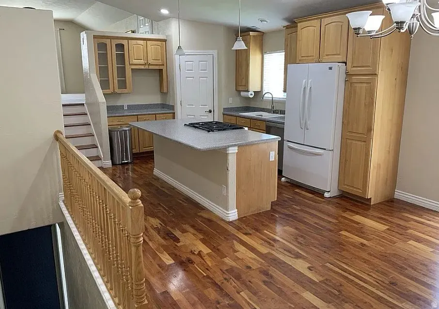 Kitchen featuring wood-finish flooring, light wood cabinetry, a center island with a built-in cooktop, and light-colored countertops