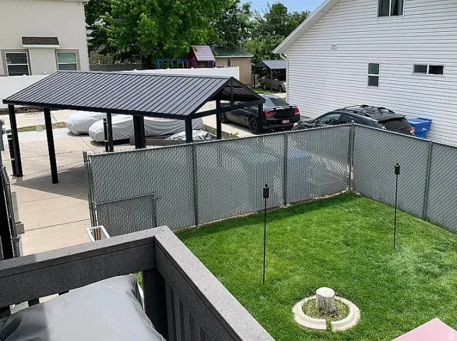 Lawn area with a tree stump feature, chain-link fencing, and a carport with a metal roof