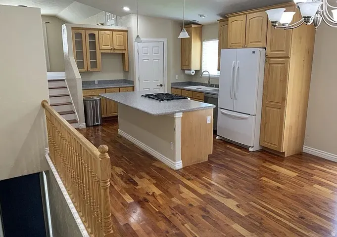 Kitchen featuring wood-finish flooring, light wood cabinetry, a center island with a built-in cooktop, and light-colored countertops