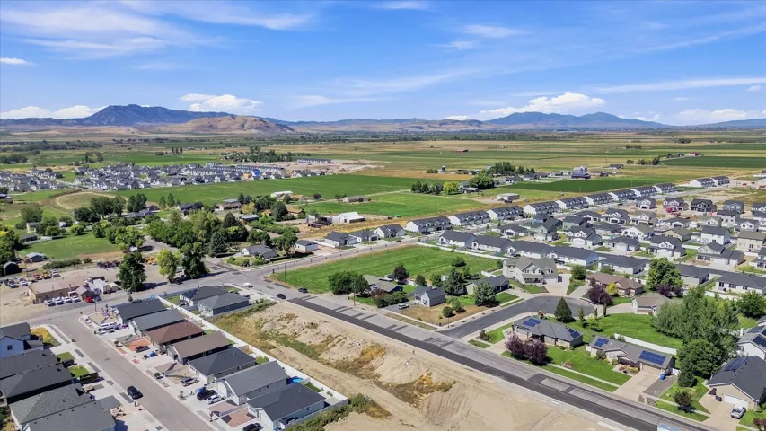 Residential area with varied home styles and green spaces, surrounded by expansive fields and distant mountains