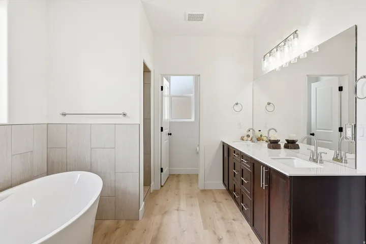 Freestanding soaking tub, wood-finish flooring, dual vanity with undermount sinks, full-width mirror, and a tiled shower stall