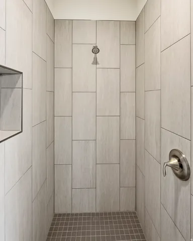 Tiled shower enclosure featuring a recessed niche, brushed nickel shower head, and coordinating fixture