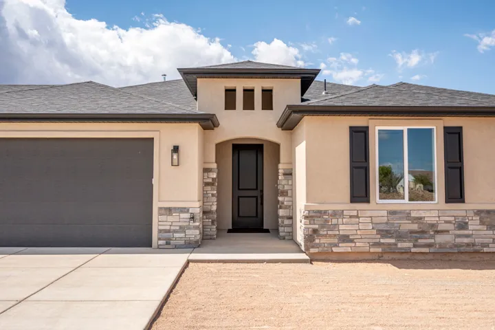 Stucco exterior with stone veneer accents, dark garage door, black front door, and an exterior light fixture