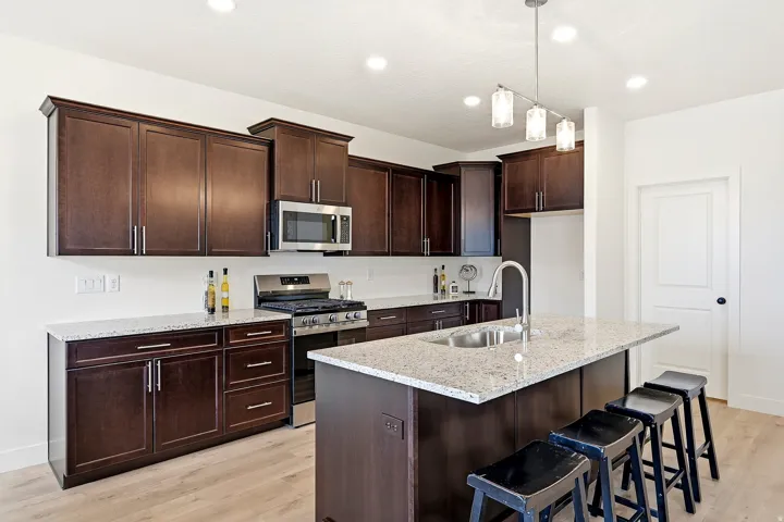Kitchen featuring dark wood-finish cabinetry, light-toned countertops, stainless steel appliances, a center island with sink, and wood-finish flooring