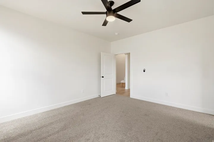 Spacious room featuring neutral carpeting, a modern ceiling fan with lighting, and white interior doors with dark hardware