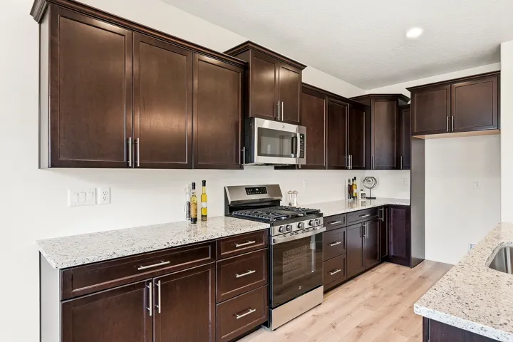 Kitchen featuring dark wood-finish cabinetry, light-toned countertops, stainless steel appliances, and wood-finish flooring