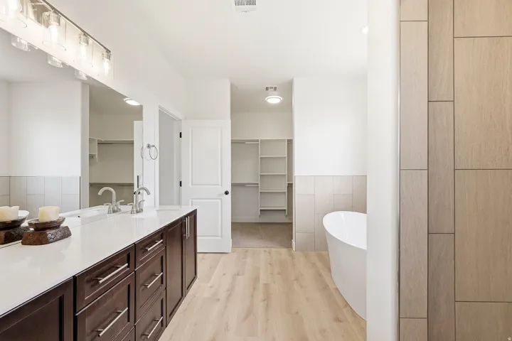 Dual vanity with an expansive countertop, dark wood-finish cabinetry, a freestanding soaking tub, wood-finish flooring, and two walk-in closets with built-in shelving