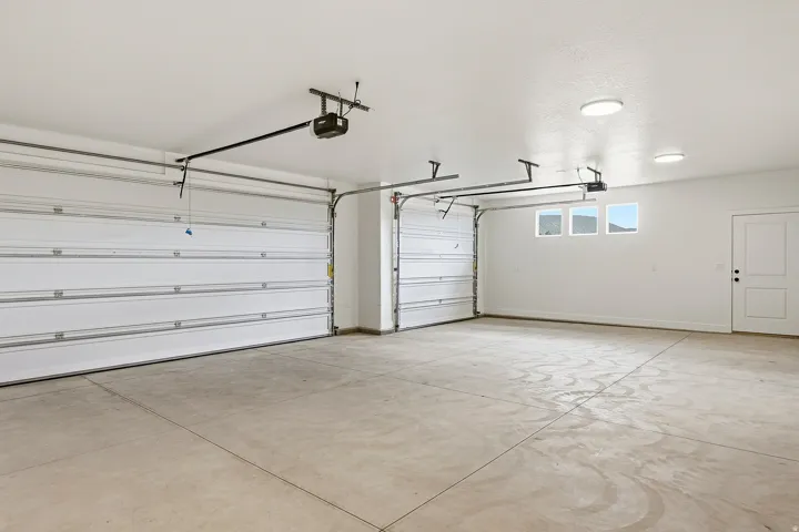 Spacious garage featuring two overhead doors with automatic openers, concrete flooring, and three high windows providing natural light