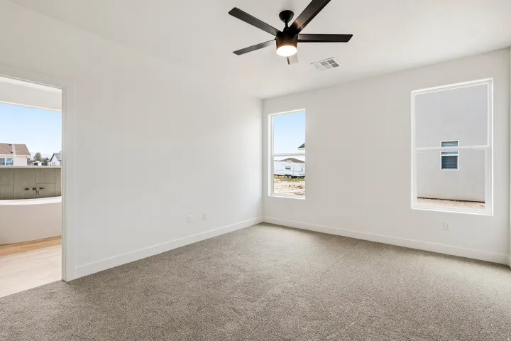 Carpeted room featuring a ceiling fan with integrated lighting, two windows, and a doorway opening to an adjacent space with wood-finish flooring