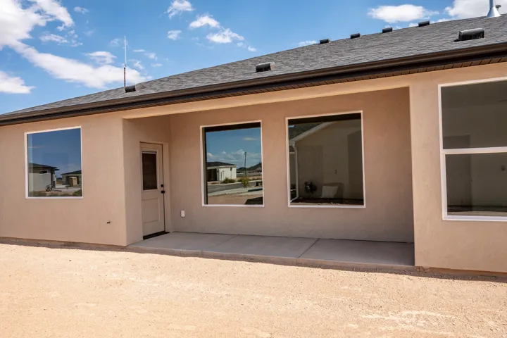 Stucco exterior with a covered concrete patio, multiple windows, and a dark shingle roof
