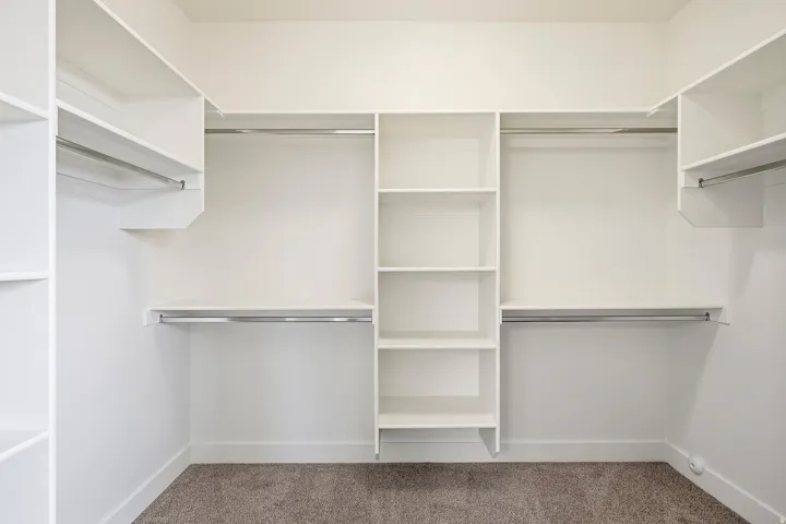 Walk-in closet with built-in shelving, multiple hanging rods, and carpet flooring