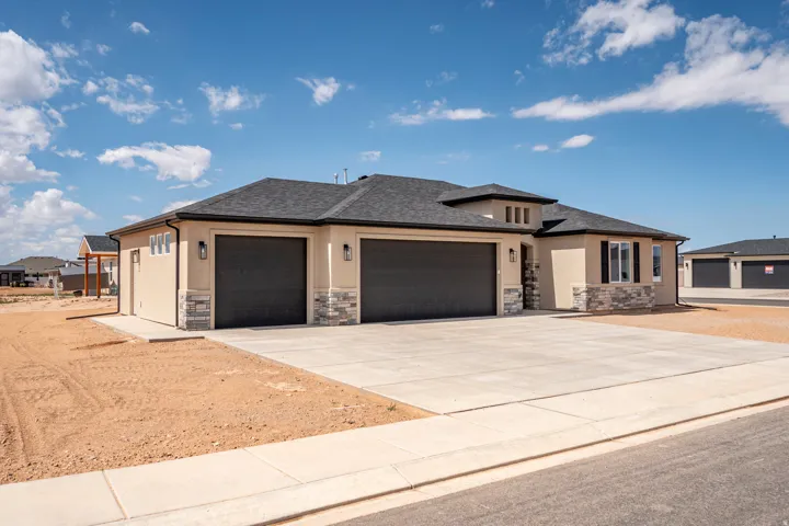 Stucco exterior with stone accenting, dark asphalt shingle roof, two garage doors, and a concrete driveway