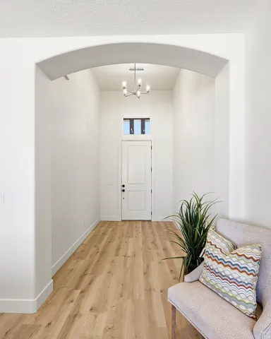 Arched entryway leading to a solid panel door with transom window, wood-finish flooring, and a contemporary chandelier