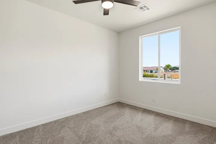Neutral wall paint throughout, plush carpet flooring, a contemporary ceiling fan with integrated lighting, and a large window providing ambient light