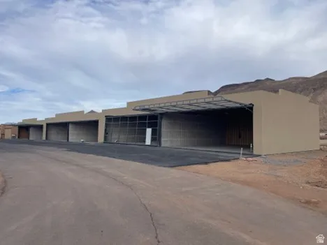 Exterior stucco finish, multiple large bays with roll-up doors, paved access, and a mountain backdrop