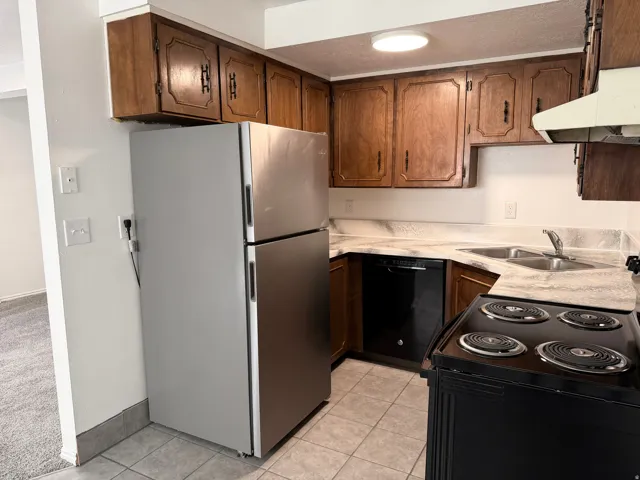 Compact kitchen featuring wood cabinetry, stainless steel refrigerator, black electric range, and a dual basin sink