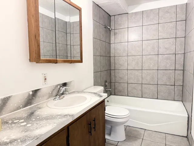 Bathroom with a built-in bathtub, tiled shower surround, integrated vanity sink, wood-finish vanity cabinetry, and a mirrored medicine cabinet