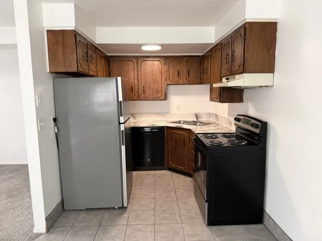 Kitchen featuring wood-finish cabinetry, tile flooring, white countertops, stainless steel sink, and black appliances