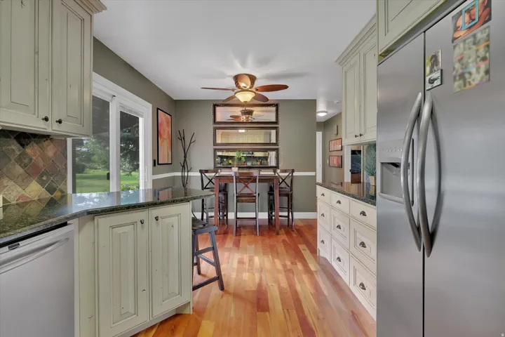 Wood-finish flooring, cream-painted cabinetry, dark stone countertops, tile backsplash, and a stainless steel refrigerator