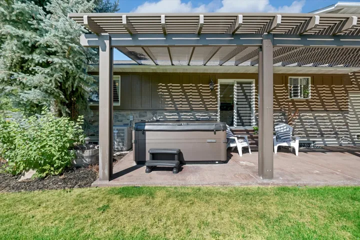 Private backyard patio featuring a pergola, spa, and mature landscaping