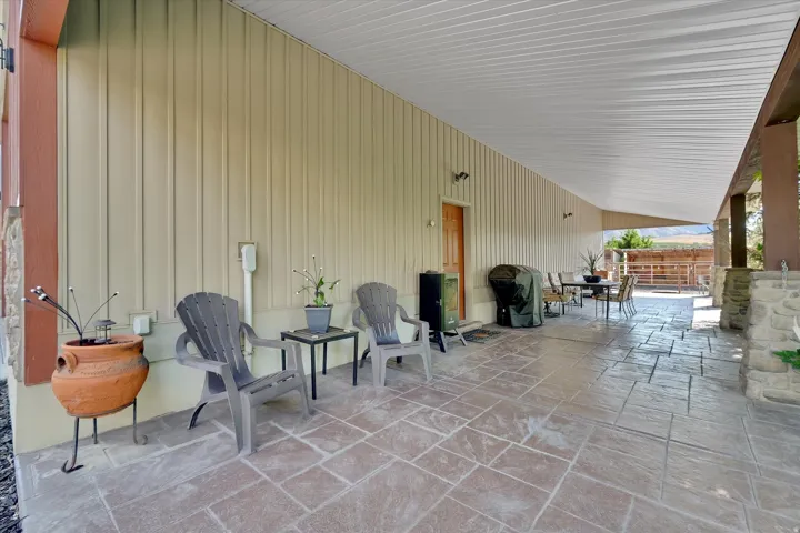 Expansive covered patio with stamped concrete flooring, corrugated ceiling, and stone-clad pillars