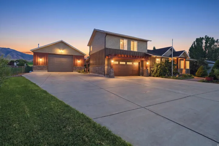 Expansive concrete driveway, attached two-car garage with pergola, separate detached garage, stone and siding exterior, and well-maintained landscaping