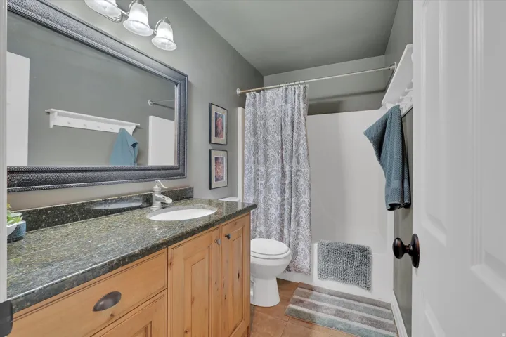 Bathroom featuring a natural wood vanity with dark stone countertop, integrated sink, and framed mirror