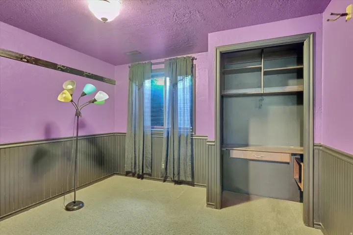 Built-in shelving with integrated desk, window with blinds, wall-mounted light fixture, and wainscoting