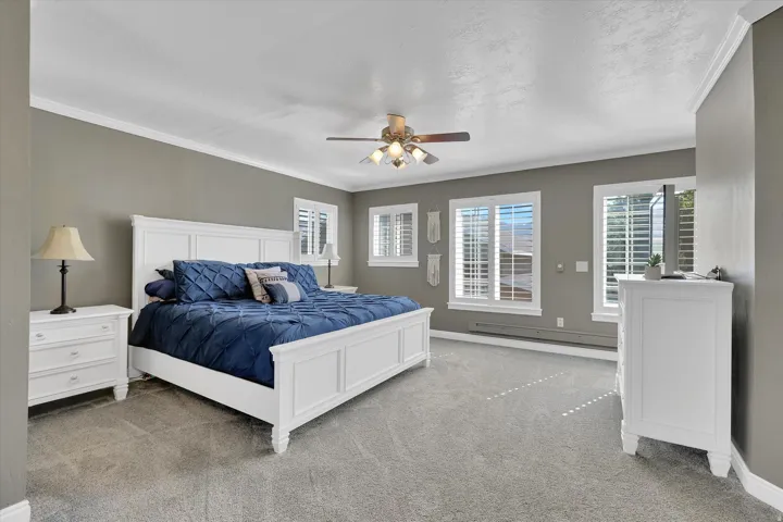 Spacious room featuring gray walls, light-colored carpeting, multiple windows with plantation shutters, and a ceiling fan with integrated lighting