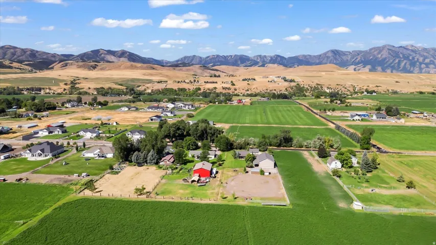 Expansive green fields with distant mountains under a blue sky, featuring multiple residential properties and a red barn