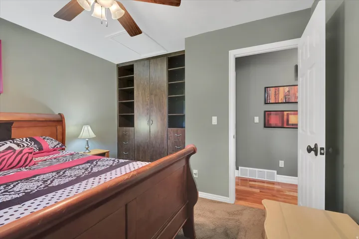 Built-in closet system with shelving and storage, wood-finish ceiling fan, and carpeted flooring