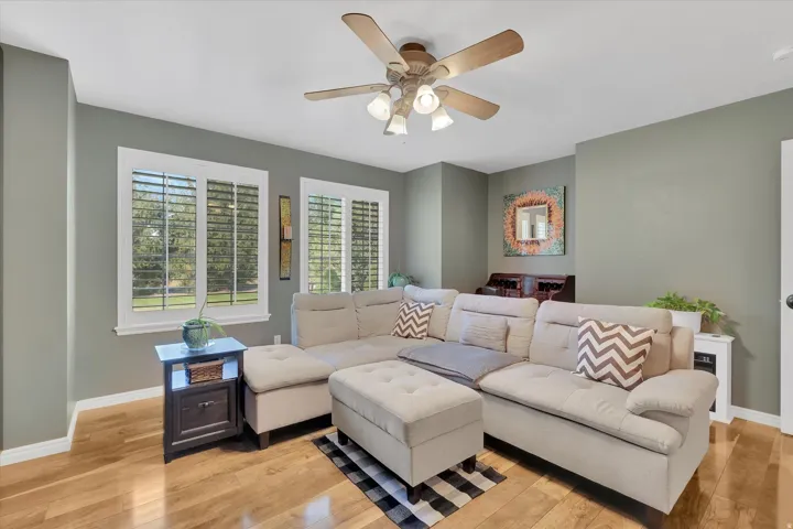 Wood-finish flooring, multiple windows with white plantation shutters, ceiling fan with integrated lighting, built-in desk, and recessed wall paneling