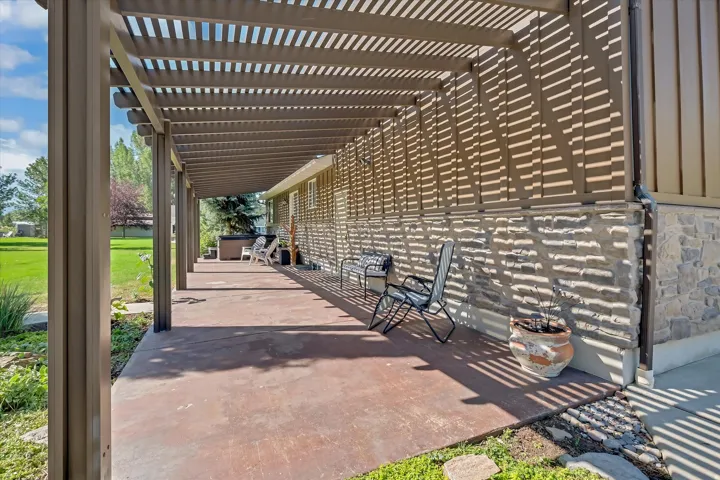 Spacious covered patio with concrete flooring, supported by multiple columns, and featuring a stone facade