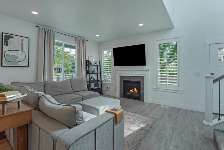 Living space featuring a fireplace with a stone surround, wood-finish flooring, recessed lighting, and large windows with plantation shutters