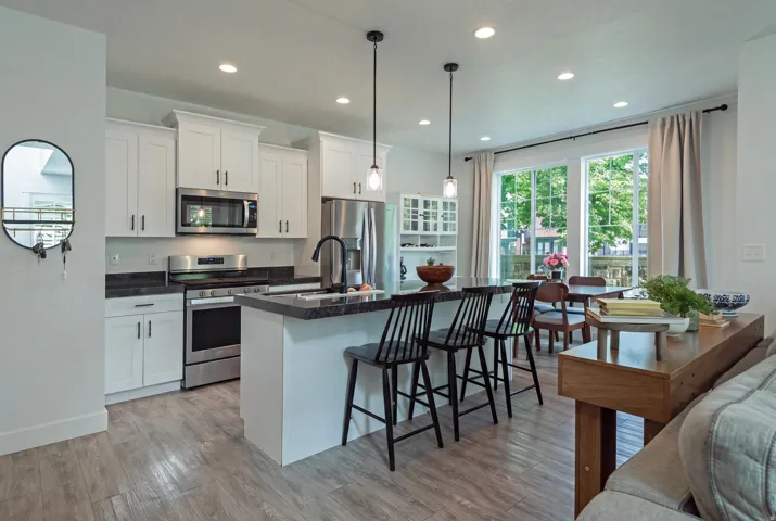 Modern kitchen featuring white cabinetry, stainless steel appliances, dark countertops, a central island with pendant lighting, and wood-finish flooring