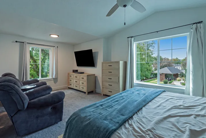 Vaulted ceiling with a ceiling fan, dual windows, and carpeted flooring