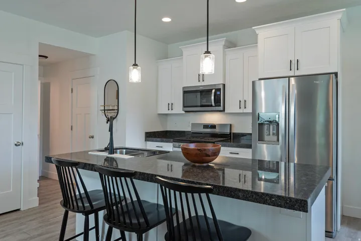 Kitchen featuring white shaker cabinetry, dark stone countertops, stainless steel appliances, and a kitchen island with seating